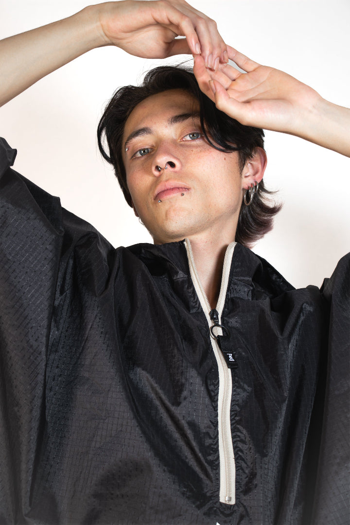 Person wearing a black jacket with a white zipper against a plain background