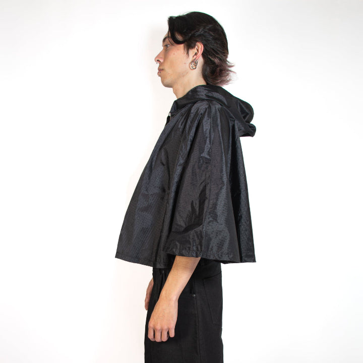 Person wearing a black hooded cape and shorts on a white background