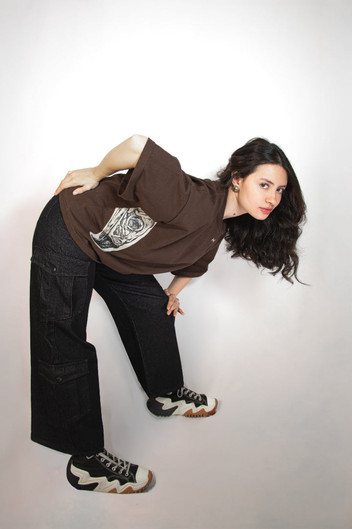 Woman posing in a brown shirt with graphic design and black pants on a white background