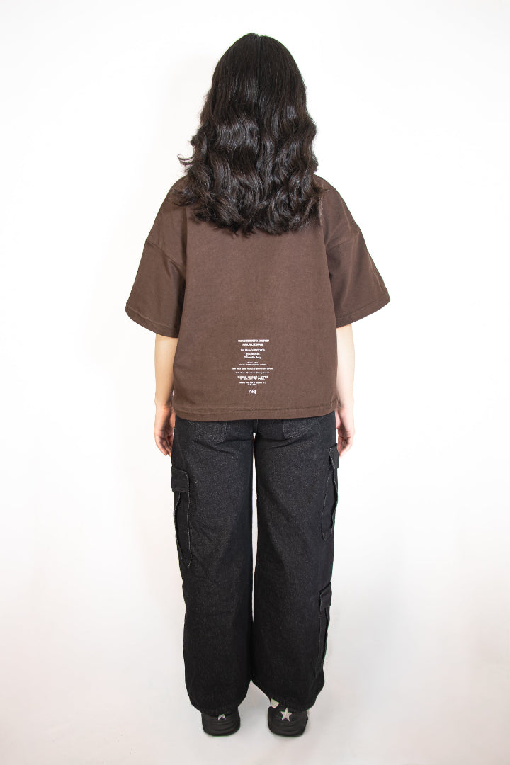 Person wearing a brown t-shirt with text on the back and black pants on a white background