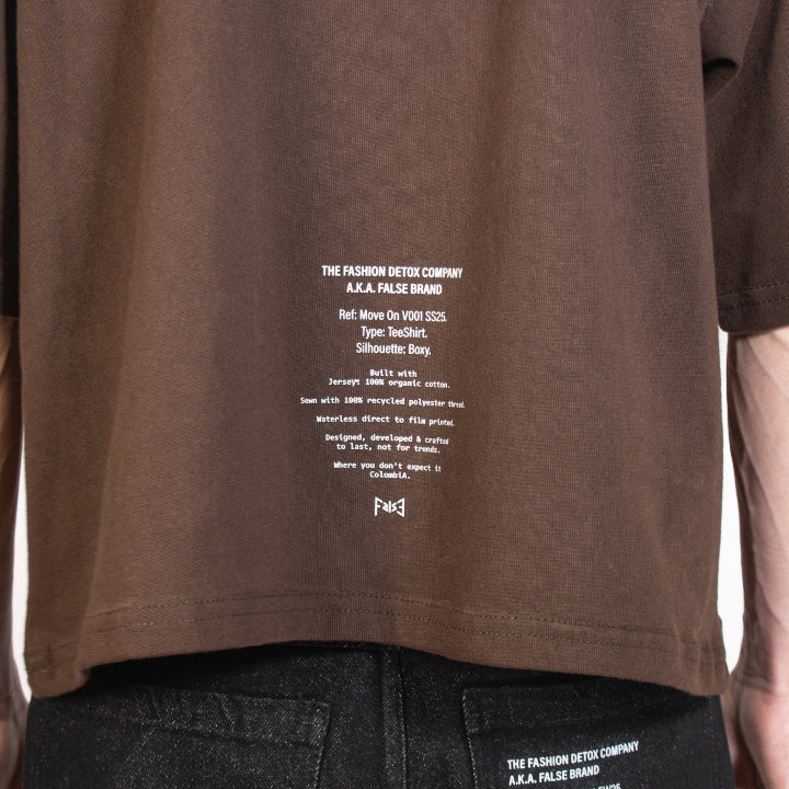 Brown t-shirt with white text on the back worn by a person, on a plain background