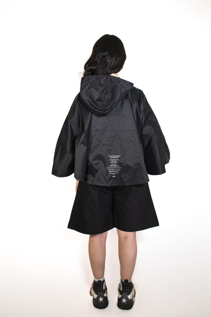 Person wearing a black hooded jacket and shorts on a white background